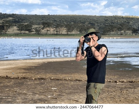 A male photographer in a green hat takes a photo the savannah on the background of Lake Nakuru, Kenya. The concept of an African safari in Africa. a photographer in nature. A naturalist shoots