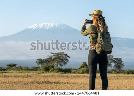 beautiful young girl In a hat stands against the backdrop of the Kilimanjaro volcano and looks away. The concept of tourism and African safari. female backpacker takes pictures of nature and animals