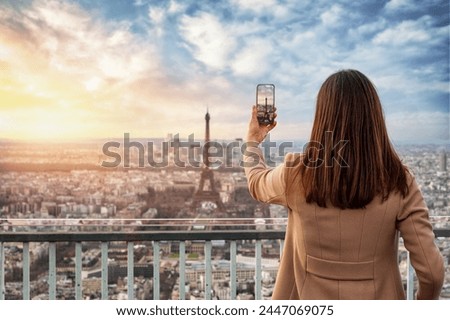 A tourist woman takes pictures with ther phone from the skyline of Paris, France, during sunset time