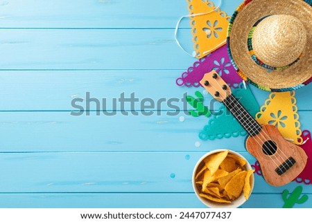 Celebrate Cinco de Mayo with this colorful top view arrangement: sombrero, vihuela, flag garland, nachos on wooden blue backdrop. Ideal for promotional materials