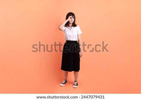 Cheerful female student in Thai university uniform with gesture of looking far away isolated on orange background. International Students' Day, World Students' Day. Gen Z