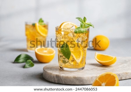 Two glasses with iced drink with lemon and mint  on a marble board on a light background with shadow and citrus fruits. The concept of a cold tea or lemonade on a hot summer day. Front view.