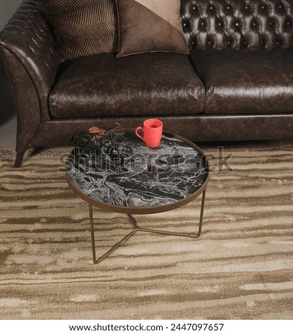 Oval side table, with black and gray marble pattern on it, gold lacquered legs, next to the armchair.
