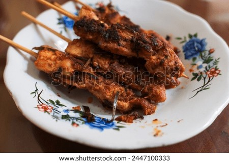 Several skewers "sate" of chicken meat in a white plate on a wooden table, traditional meal, Indonesian food, stock photo.