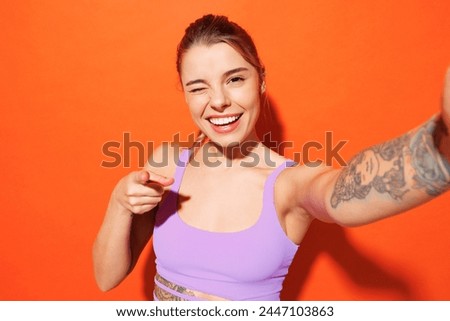 Young fitness trainer woman sportsman wear purple top clothes in home gym do selfie shot mobile cell phone point finger camera on you isolated on plain orange background. Workout sport fit abs concept