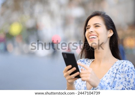 Happy woman laughing looking above holding phone in the street