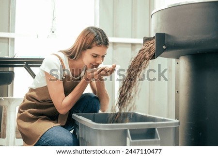 White Woman craftsperson observing and checking quality of Freshly roasted coffee beans being removed from the roaster into the plastic keeper.. Royalty-Free Stock Photo #2447110477