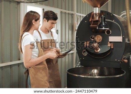 White Man and Woman craftspersons observing and checking quality of Freshly roasted coffee beans being removed from the roaster into the cooling cylinder. Royalty-Free Stock Photo #2447110479
