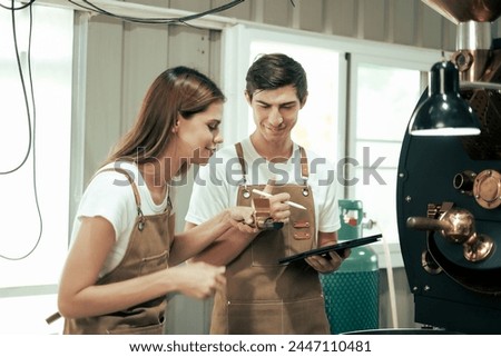 White Man and Woman craftspersons observing and checking quality of Freshly roasted coffee beans being removed from the roaster into the cooling cylinder. Royalty-Free Stock Photo #2447110481