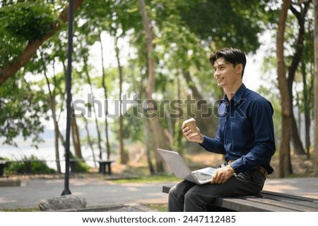 Portrait of attractive businessman sitting on a park bench and working with laptop
