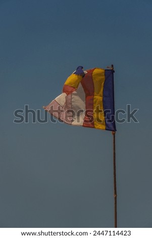A flag with a blue stripe and red and yellow stripes is blowing in the wind. The flag is on a pole and is flying high in the sky