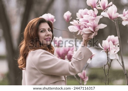 Woman magnolia flowers, surrounded by blossoming trees., hair down, wearing a light coat. Captured during spring, showcasing natural beauty and seasonal change.