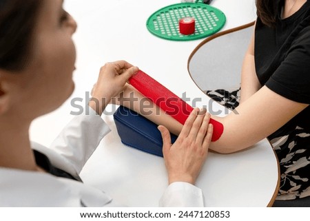 Physical therapist placing kinesio tape on patient's elbow. Therapy with kinesio tex tape. Therapeutic treatment of elbow with kinesio tape. kinesio treatment after sports muscle injury.  Royalty-Free Stock Photo #2447120853
