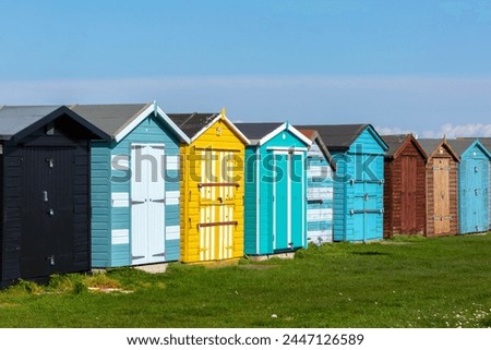 Beach huts along the Essex coast, Image shows a range of different colours and styles of beach huts on a warm spring day with slight cloud and blue sky Royalty-Free Stock Photo #2447126589
