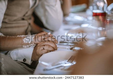 Valmiera, Latvia - Augist 13, 2023 - 
Close-up of clasped hands at a dining table, with a focus on a lace sleeve and wedding ring. Royalty-Free Stock Photo #2447127383