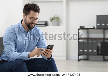 Handsome young man using smartphone in office, space for text