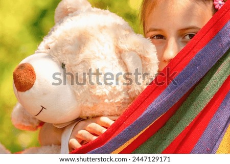 Summer holiday and resting concept. Portrait of young beautiful girl with toy Teddy bear resting in hammock at green garden. 