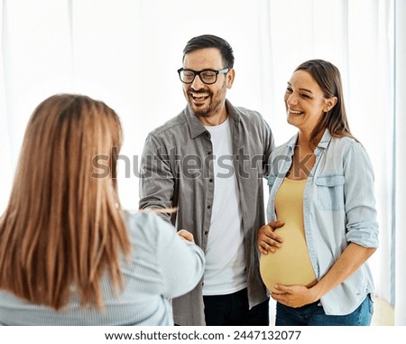 Young happy couple, a pregnant woman, and an agent shaking hands in a new property