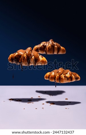 Chocolate-covered croissant clouds floating and dripping on blue background Royalty-Free Stock Photo #2447132437