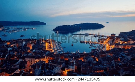 Birds eye view of the evening city during sunset. Aerial photography. Lights on lanterns on dusk. The ships are in the bay. Tiled roofs of houses in the old town. Rovinj, Croatia - April 7, 2024