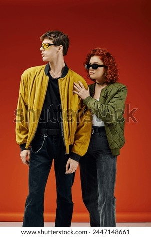 loving debonair couple in fancy sunglasses in trendy attires posing together on red backdrop Royalty-Free Stock Photo #2447148661