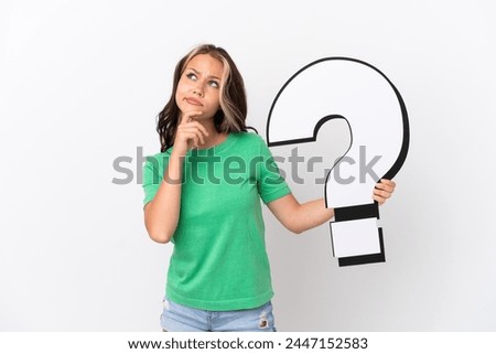 Teenager Russian girl isolated on blue background holding a question mark icon and having doubts