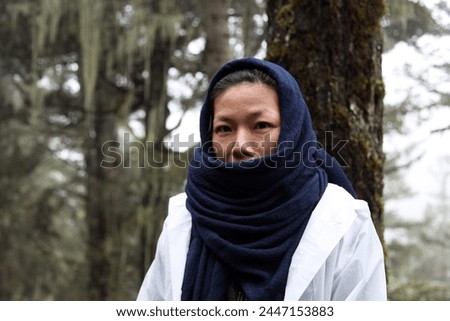 Exterior photo portrait view of a young Asian Chinese female woman who is pretty beautiful charming in her 30s wearing a dark blue scaf to preotect from the fresh cold weather in the forest air