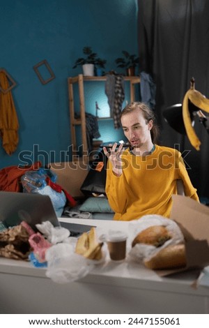Young man working studying in messy room dictate voice message on smartphone