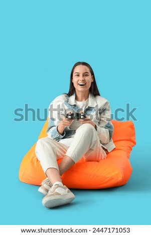 Beautiful young happy woman playing video games on beanbag chair against blue background