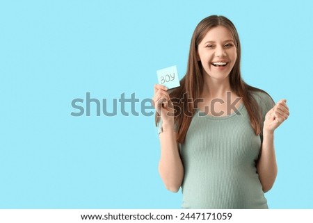 Happy pregnant woman holding paper with word BOY on blue background