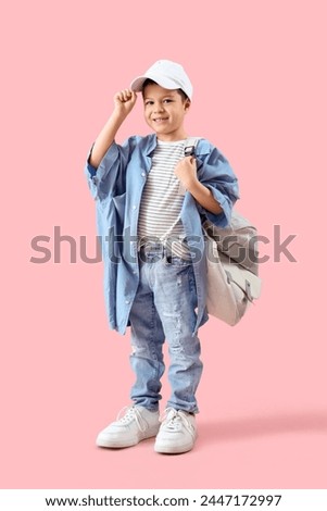 Cute little Asian boy in adult clothes with backpack on pink background