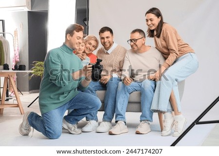 Male photographer showing pictures to big family on sofa in studio