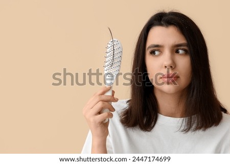 Stressed young woman with hair loss problem on beige background