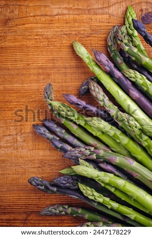 Raw green and violet asparagus beaded in a row in cinematic look as top view on rustic wooden board with copy space on top 