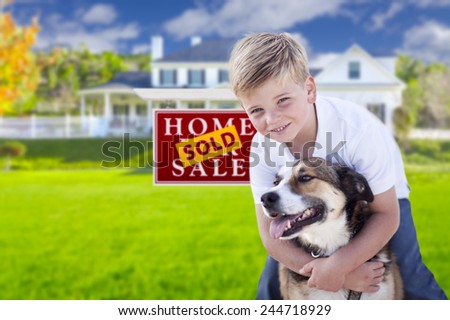 Happy Young Boy and His Dog in Front of Sold For Sale Real Estate Sign and House.