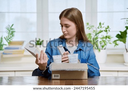 Young female customer sitting at home unpacking cardboard box with online purchases Royalty-Free Stock Photo #2447195455
