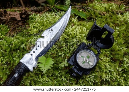 Old compass and hunting knife on green moss covered wood. direction finder compass. Aiming compass
