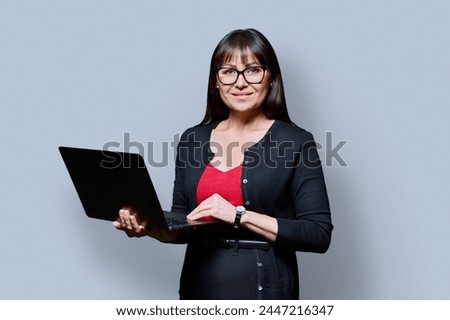 Smiling business middle aged woman using laptop on gray background