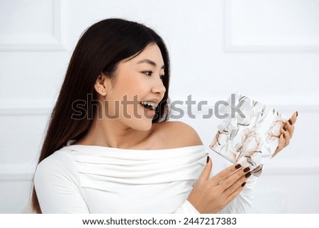 Amazed asian woman holding gift and looking on it with surprised face while celebrating birthday at home. Holidays concept