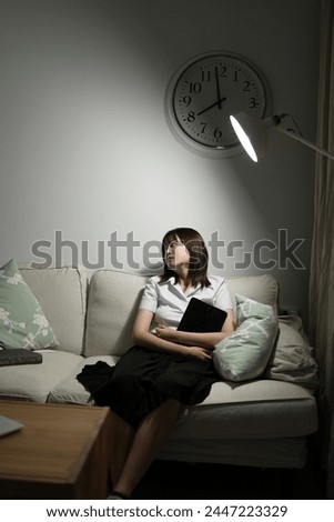 A young female student in a Thai university uniform sits on a sofa in the living room, Waiting for her parent. International Students' Day, World Students' Day. Gen Z