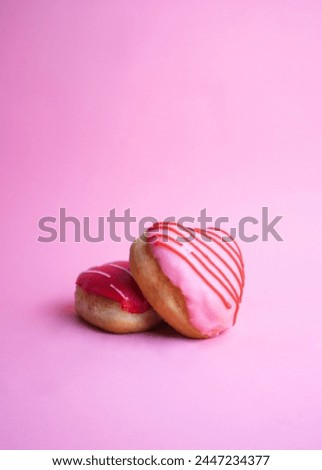 heart-shaped filled doughnut with pink and red icing on a pink background