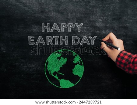 A person is writing on a chalkboard with a marker. The chalkboard says Happy Earth Day