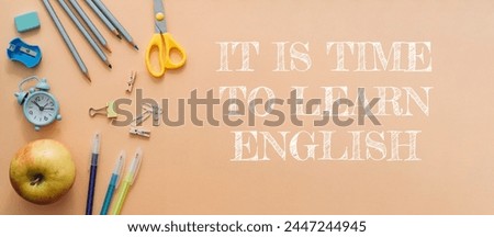 A bunch of school supplies and a clock on a table with the words It is time to learn English written below
