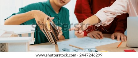 Smart interior designer compares color between color swatches and house model on meeting table with house model and architectural document scatter around. Creative working concept. Variegated