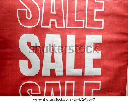 A red sign with white letters that say "SALE" on it. The sign is hanging on a wall