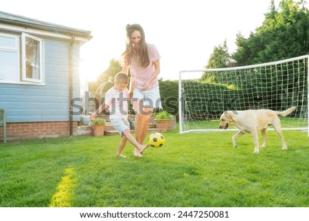 Young mother and son plays soccer with dog and have fun together. Happy family playing football with pet. Fun Playing Games in Backyard Lawn on Sunny Summer Day. Motherhood, childhood, togetherness Royalty-Free Stock Photo #2447250081
