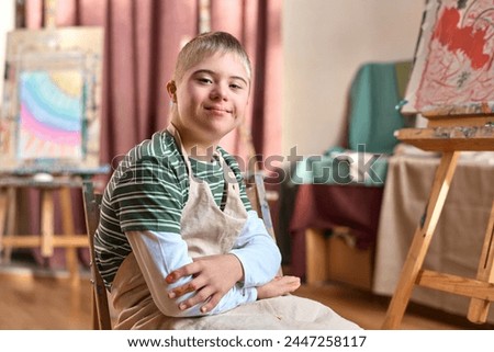 Portrait of smiling teen boy with Down syndrome smiling at camera in art studio copy space