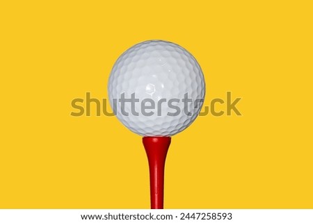 Image of a golf ball set on a red tee with a yellow isolated background.