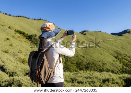 Hiking woman enjoy the beautiful view and use of mobile phone to take photo at mountain peak 
