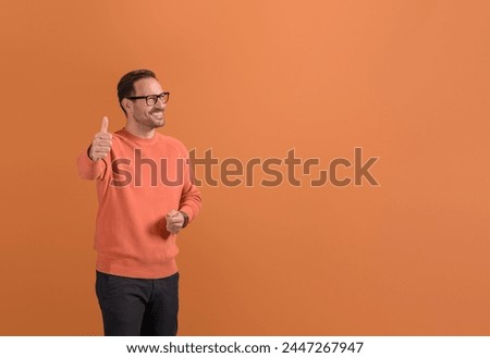 Portrait of happy male entrepreneur showing thumbs up sign and looking away on orange background